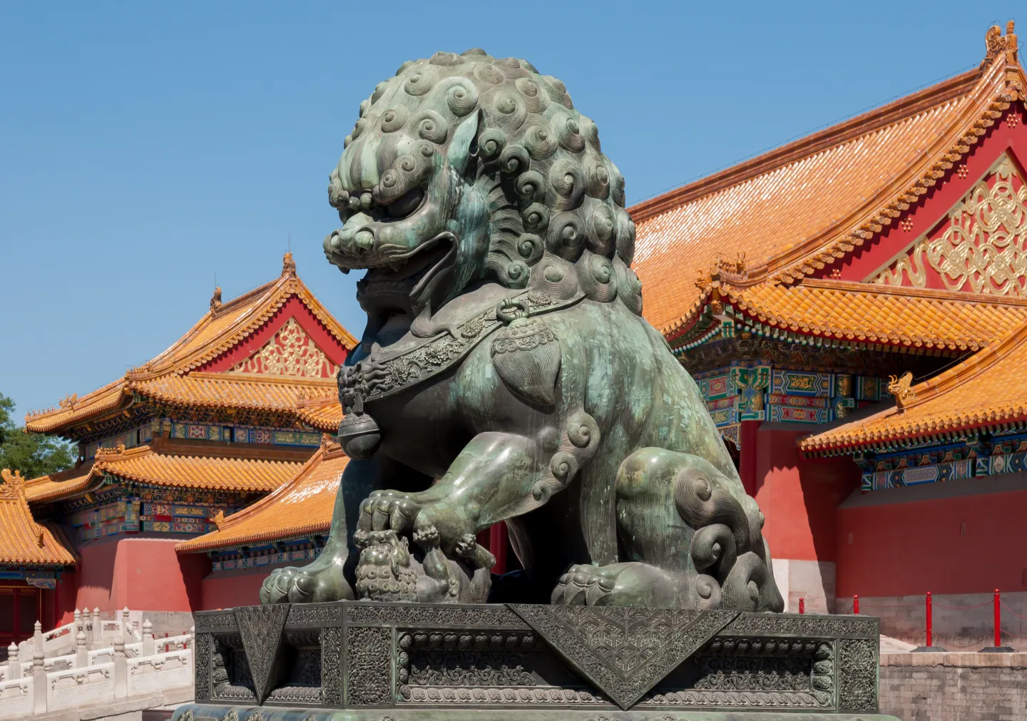 Bronze lion with the golden roofs of the Gate of Supreme Harmony behind it